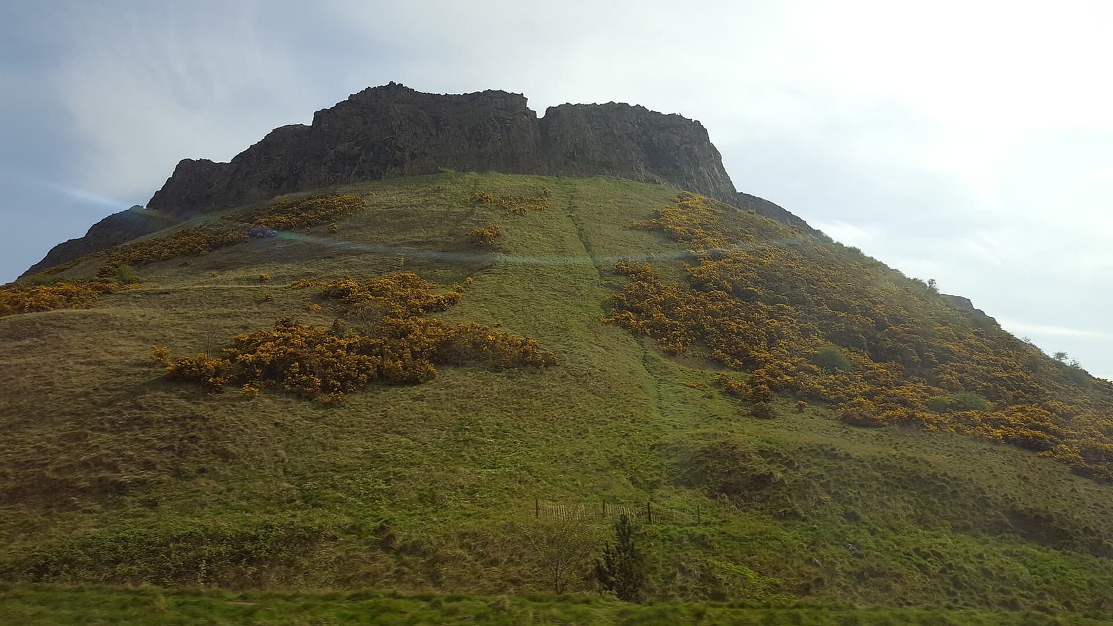 The dark cliffs of Salisbury Crags above a grassy slope dotted with yellow gorse