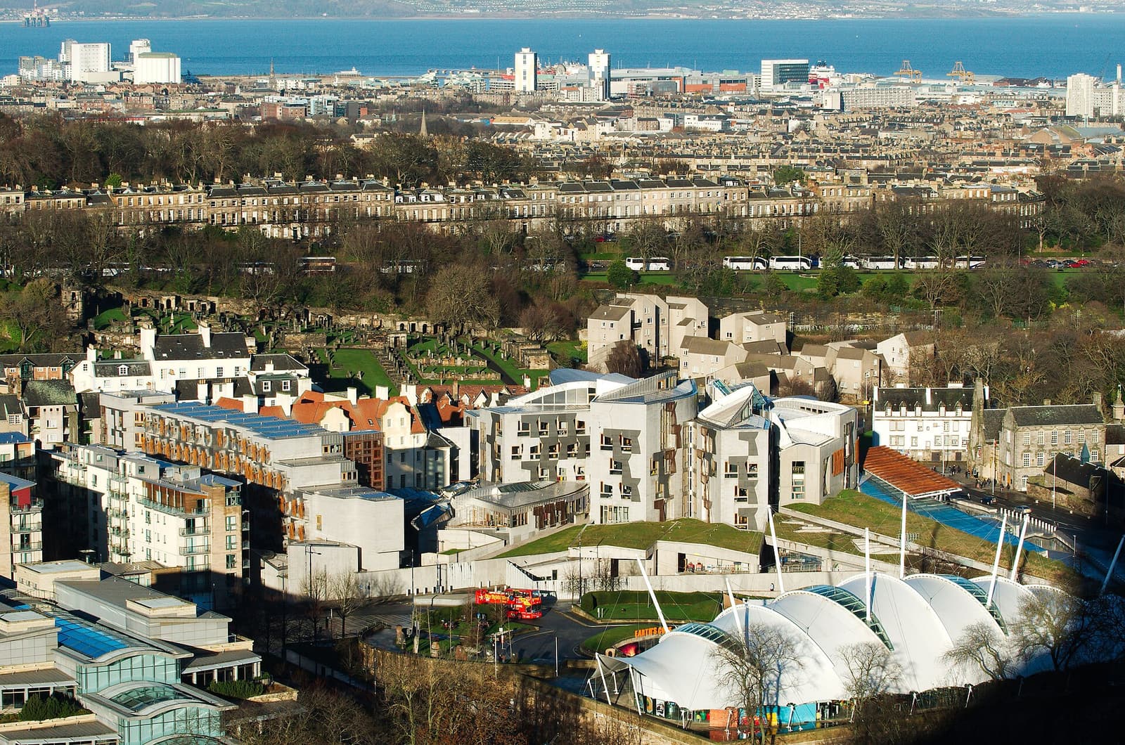 The Scottish Parliament and the white tented roof of Dynamic Earth seen from Salisbury Crags, with the Firth of Forth beyond