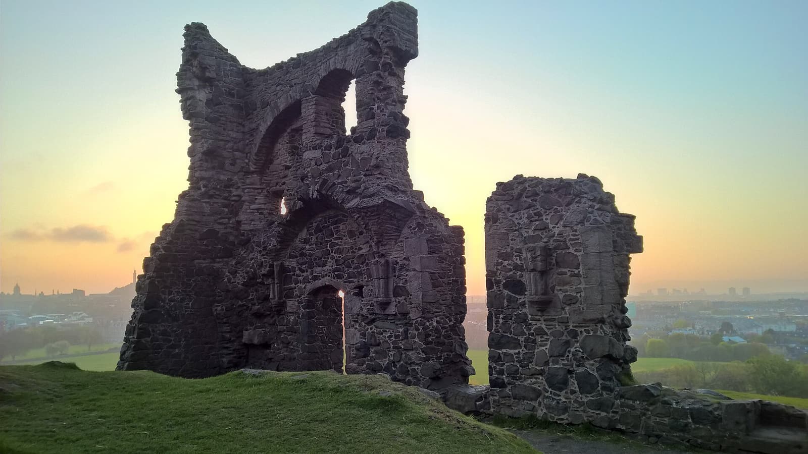 The ruined stone walls of St Anthony’s Chapel on its hilltop at sunset