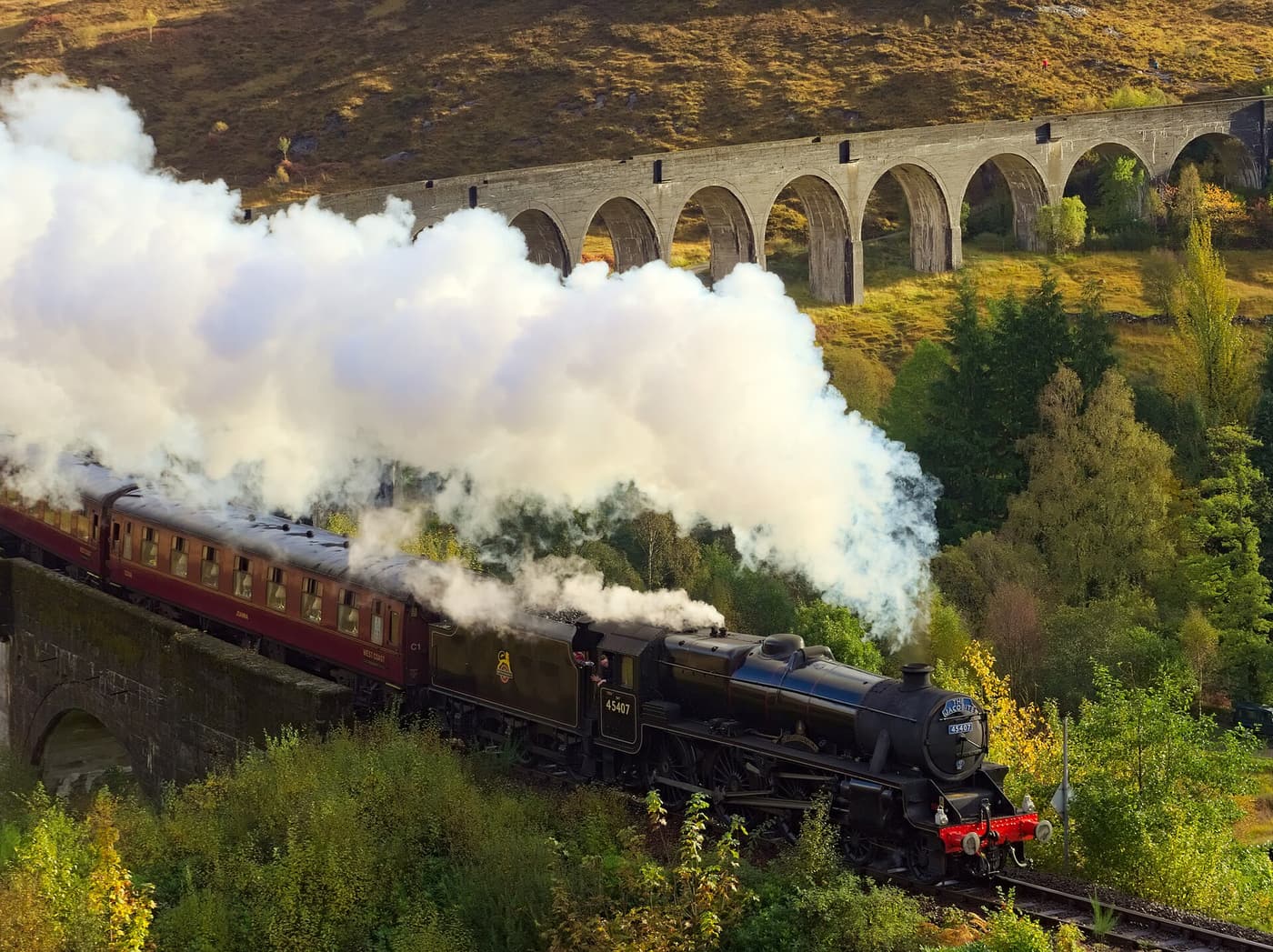 A steam train crossing the curved stone arches of the Glenfinnan Viaduct