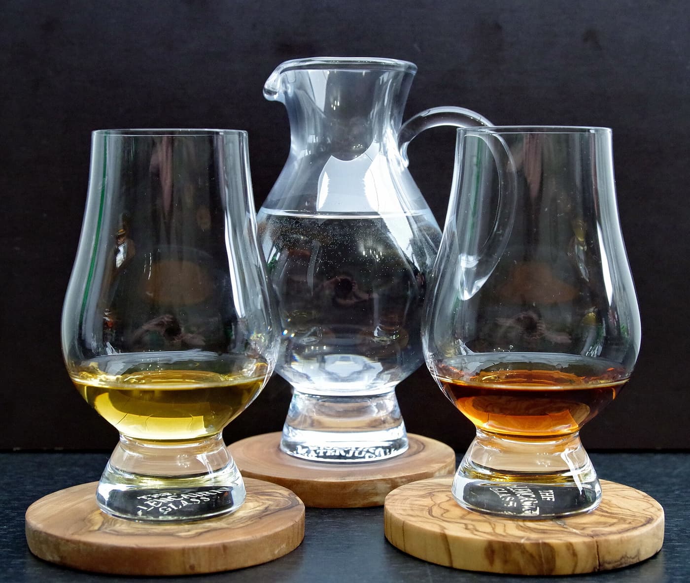 Two tulip-shaped whisky tasting glasses and a small water jug on wooden coasters